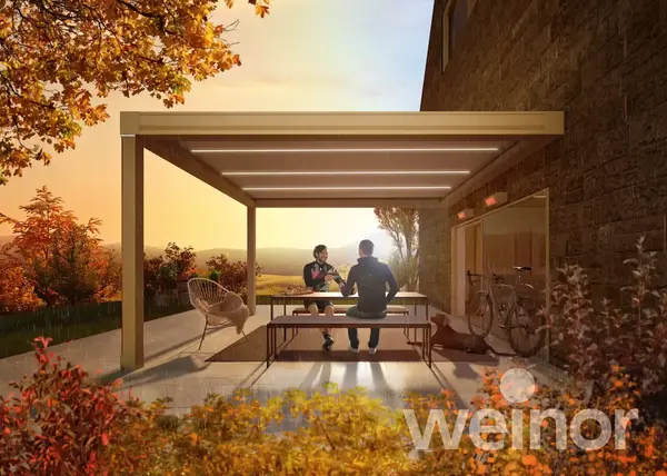 LED-Terrassenüberdachung am Haus, zwei Personen sitzen im Herbstgarten