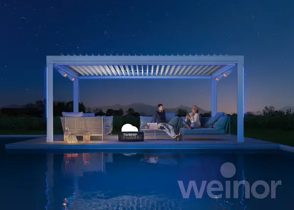 Beleuchtete Pergola mit Lamellendach am Pool, Lounge im Garten bei Nacht